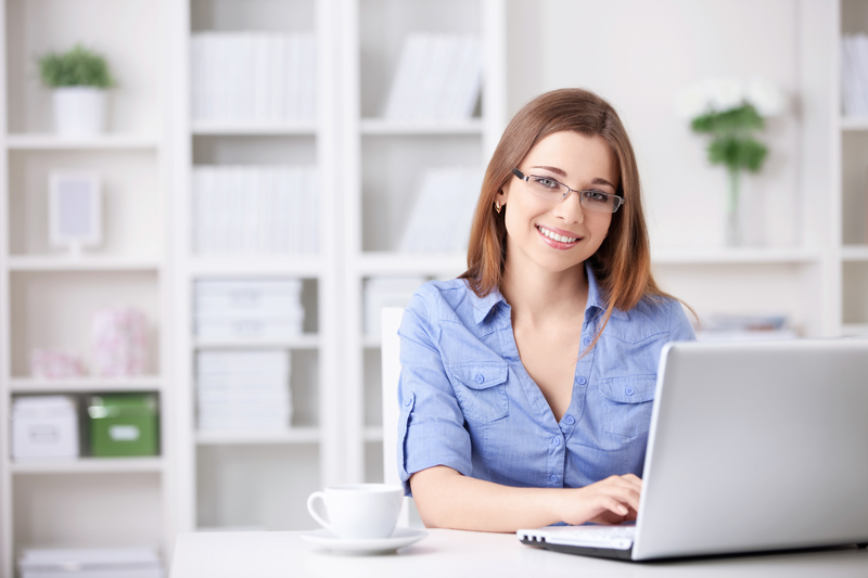 A cheerful office worker at a laptop in a bright office setting.